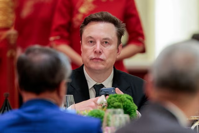 Tesla CEO Elon Musk holds a mobile phone as he arrives to attend a state banquet with U.S. President Donald Trump and Chinese President Xi Jinping at the Great Hall of the People in Beijing, China, May 14, 2026. REUTERS/Evan Vucci