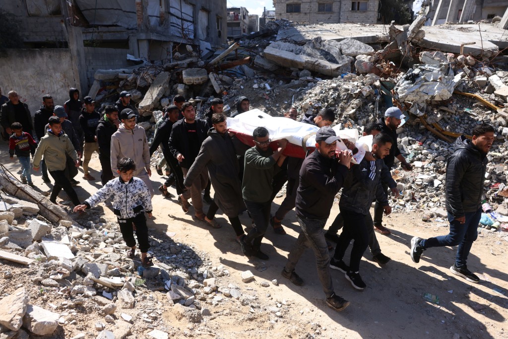 Photo by BASHAR TALEB / AFP  Palestinian men carry the body of a person killed in an Israeli military strike, as they maneuvre past the debris of building destroyed by the Israeli military, during their funeral in Khan Yunis, in the southern Gaza Strip on February 27, 2026.