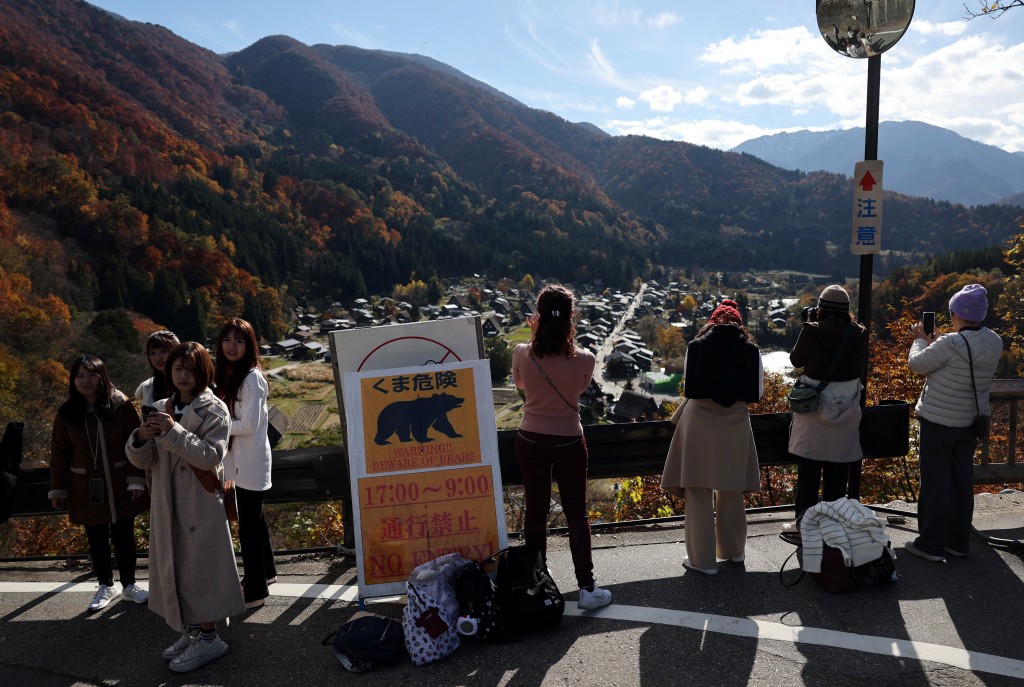 Visitors take souvenir photos next to a bear warning sign at Shirakawa-go, a popular tourist spot and one of Japan's UNESCO World Heritage sites, in Shirakawa village, Gifu Prefecture, Japan, November 15, 2025. REUTERS/Issei Kato