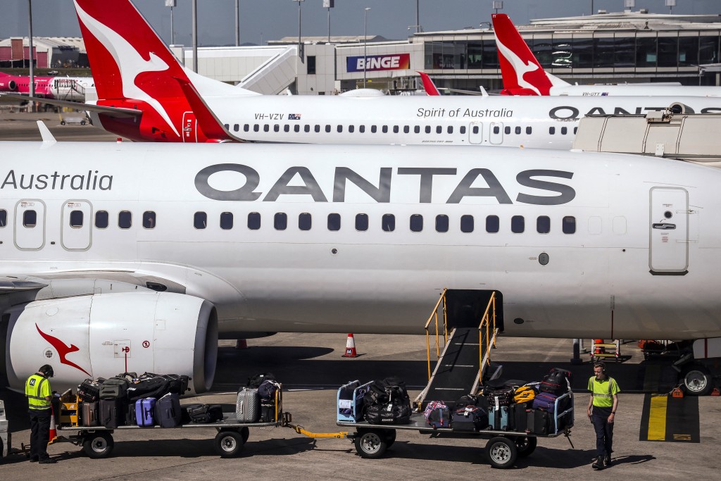 Photo by DAVID GRAY / AFP  This photo taken on August 25, 2025 shows Qantas Airways ground staff loading luggage onto a Boeing 737 aircraft on the tarmac of Brisbane Airport in Queensland.