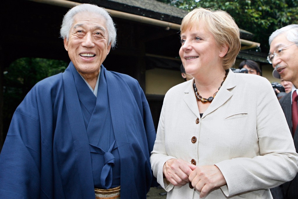 This file photo taken on August 31, 2007 shows then-German Chancellor Angela Merkel (R) sharing a light moment with Sen Genshitsu (L), head of the Urasenke school during her visit in Kyoto. Sen Genshitsu, the 15th generation headmaster in Japan's "Urasenke" tea tradition, has died at age 102, local reports said on August 14, 2025. (Photo by TORU YAMANAKA / POOL / AFP)