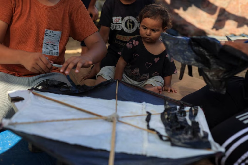 A child looks on as Palestinians make a kite at a tent camp sheltering displaced people in Gaza City, August 25, 2026. REUTERS/Dawoud Abu Alkas