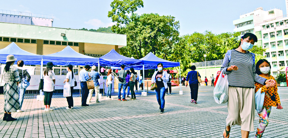 People queue at a testing center as beds are prepared at Asia World-Expo, which will admit patients in stable condition, says Linda Yu, inset. SING TAO People queue at a testing center as beds are prepared at Asia World-Expo, which will admit patients in stable condition, says Linda Yu, inset. SING TAO