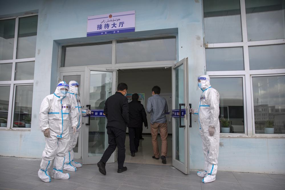 Security officers in protective suits hold the doors as government officials enter the visitors' hall at the Urumqi No. 3 Detention Center in Dabancheng in western China's Xinjiang Uyghur Autonomous Region on April 23, 2021.