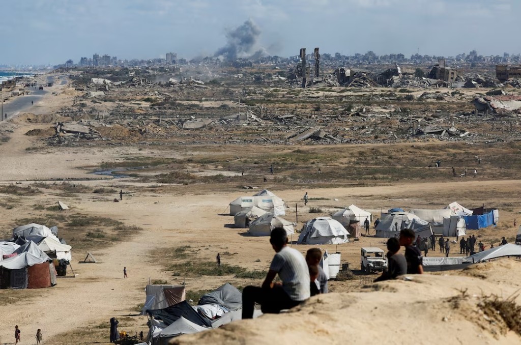 Palestinians look on as smoke rises following explosions in Gaza City, as seen from central Gaza Strip October 5, 2025. REUTERS/Mahmoud Issa