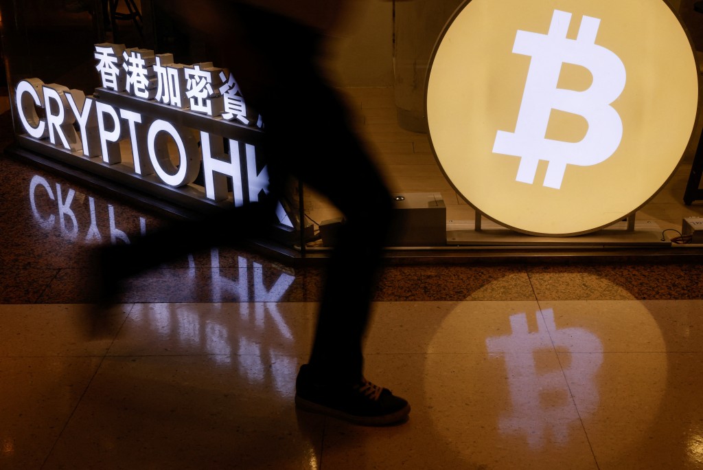 A man rushes past a cryptocurrency exchange store after Bitcoin soars above $100,000, in Hong Kong, China December 5, 2024. REUTERS/Tyrone Siu