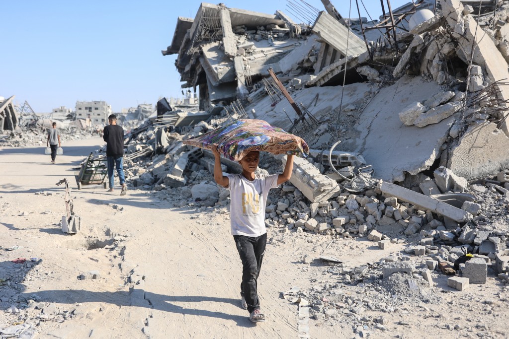 A Palestinian boy carrying belongings walks past the rubble of destroyed buildings in the al-Tuffah neighbourhood of Gaza City on October 27, 2025. (Photo by Omar AL-QATTAA / AFP)