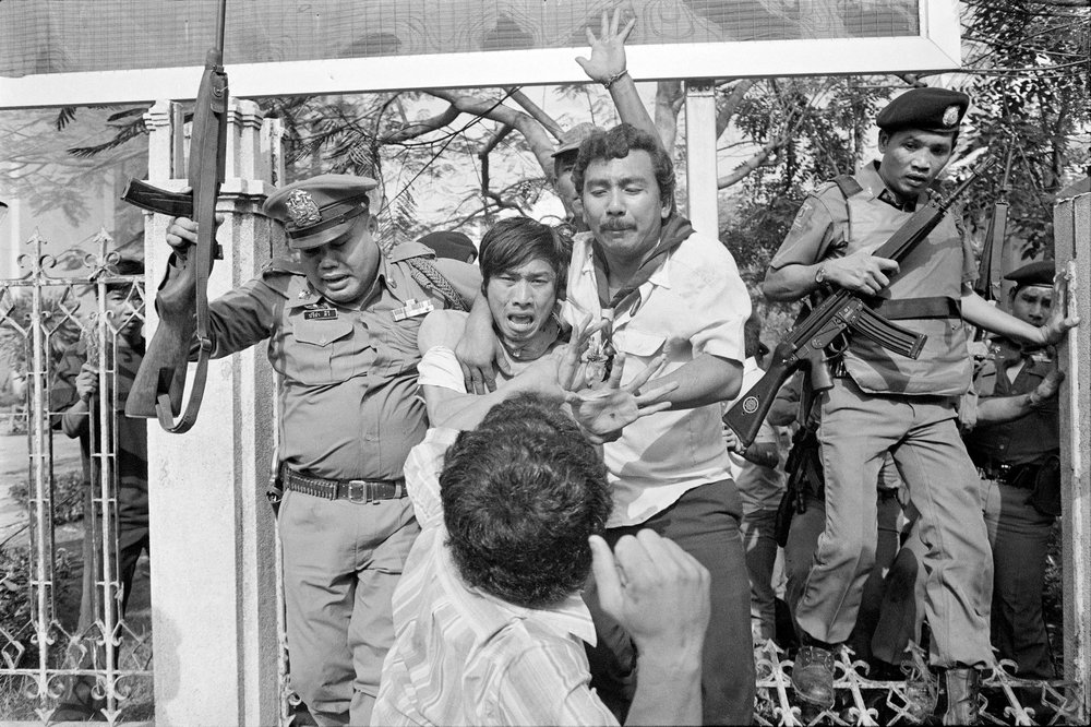 In this October 6, 1976, file photo, a right-wing student, center foreground, draws his arm back to strike a captured and wounded leftist student being taken by police to an ambulance in during a student massacre in Bangkok, Thailand. In this October 6, 1976, file photo, a right-wing student, center foreground, draws his arm back to strike a captured and wounded leftist student being taken by police to an ambulance in during a student massacre in Bangkok, Thailand.