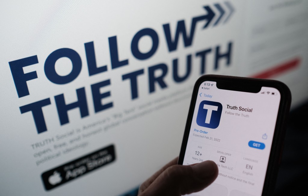 This illustration photo shows a person checking the app store on a smartphone for "Truth Social", with it's website on a computer screen in the background, in Los Angeles, October 20, 2021. AFP