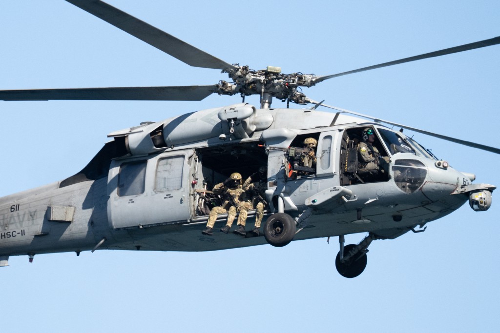 Members of the US military salute onboard a US Navy helicopter performing a fly-by for the US president and first lady as they visit the USS George H.W. Bush aircraft carrier which is out at sea near Norfolk, Virginia, October 5, 2025, during a Naval demonstration as part of the Navy's 250th anniversary celebration. (Photo by SAUL LOEB / AFP)