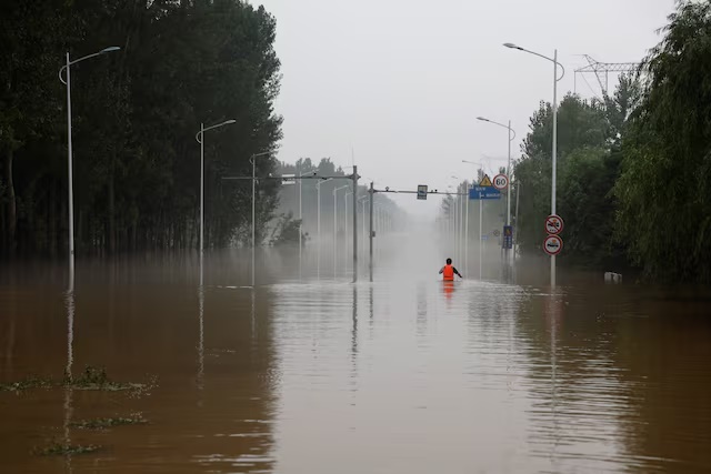 A man makes his way through a flooded road after the rains and floods brought by remnants of Typhoon Doksuri, in Zhuozhou, Hebei province, China August 3, 2023. REUTERS/Tingshu Wang