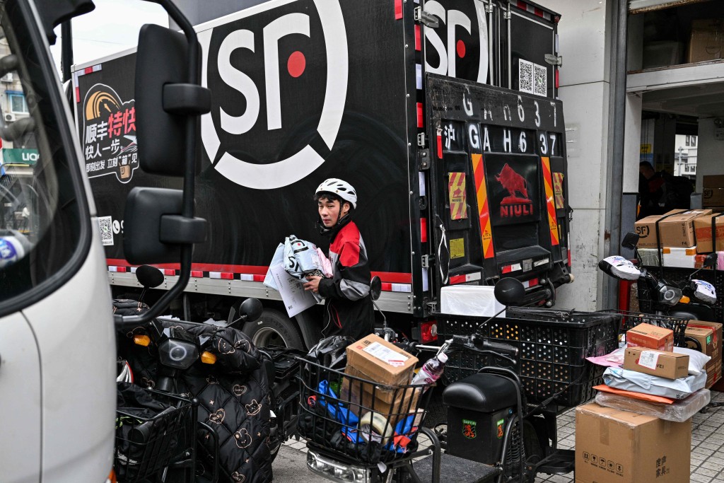 A delivery worker carries packages next to a SF Express depot during the double 11 festival or Singles Day, China's massive annual shopping event in Shanghai on November 11, 2025. AFP