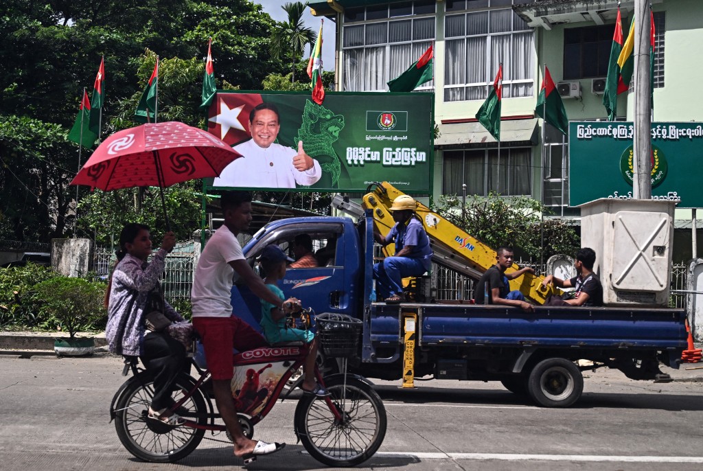 Photo by STR / AFP  People drive past an election campaign billboard of Myanmar's chairman of the army-backed ruling Union Solidarity and Development Party (USDP) Khin Yi ahead of the start of the election campaign in Yangon on October 27, 2025.