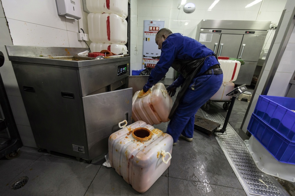 A worker collects vats of hot pot waste oil at a restaurant in Chengdu. (Bloomberg) 