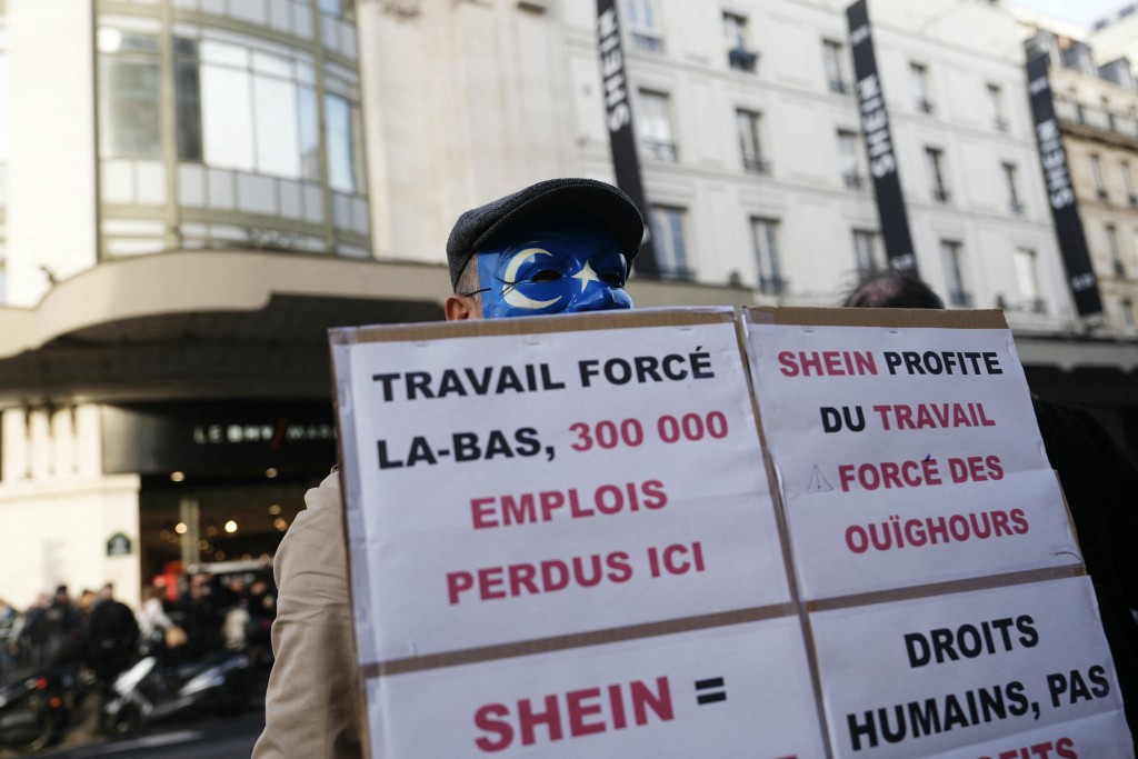 A protestor holds a banner reading "Shein profits from the forced labour of the Uyghurs" during the opening of Asian e-commerce giant Shein's first physical store at the Bazar de l'Hotel de Ville (BHV) department store in Paris on November 5, 2025. (Photo by Dimitar DILKOFF / AFP)