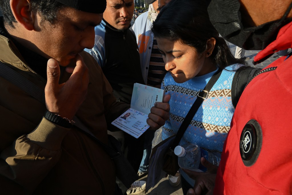 Photo by PRAKASH MATHEMA / AFP. This photograph taken on January 21, 2026 shows Lalit Bishowkarma (L), son of migrant worker Rudra Bahadur Kami, looking at his father's passport with a relative as they wait for the arrival of Kami's body outside Tribhuvan International Airport in Kathmandu.