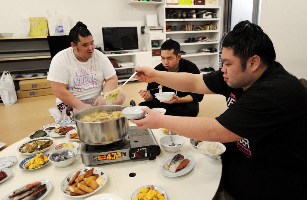 Photo by TOSHIFUMI KITAMURA / AFP  This photo taken on February 14, 2013 shows sumo wrestlers Genkaiho (R) and Migikataagari (L) having a "chankonabe" breakfast with hair dresser Tokonao (C) after a training session at a sumo stable in Tokyo.