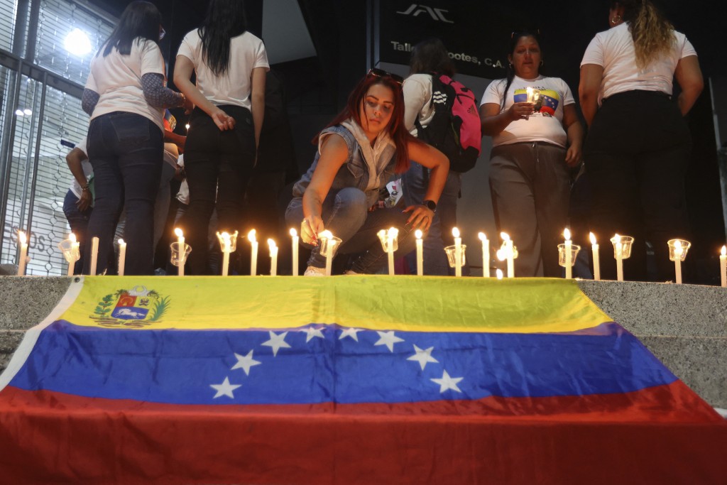Photo by PEDRO MATTEY / AFP  A woman lit a candle next to a Venezuelan flag during a vigil to demand freedom for political prisoners at El Helicoide -a facility and prison owned by the Venezuelan government and used for both regular and political prisoners of the Bolivarian National Intelligence Service (SEBIN)- in Caracas on January 13, 2026.