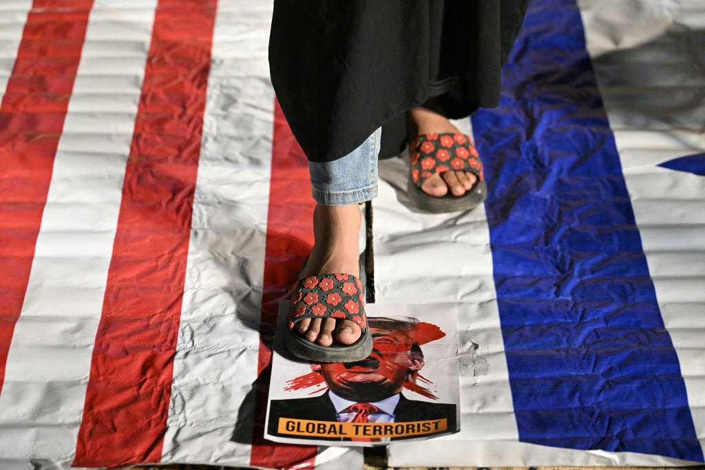 Photo by ASIF HASSAN / AFP  A Shiite Muslim stands on a portrait of US President Donald Trump with a caption reading "Global Terrorist" during celebrations after the US and Iran agreed to a two-week ceasefire in Karachi on late April 8, 2026.