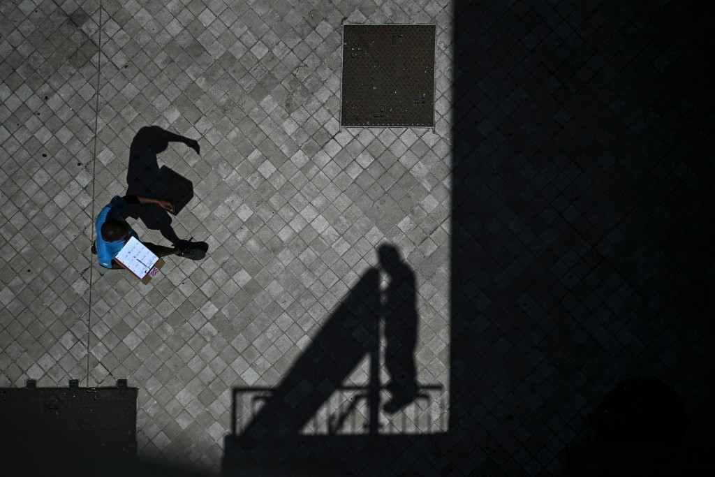 TOPSHOT - A pedestrian holds a clipboard as he walks past the shadow of a worker installing a placard at the bottom of a hotel in Bordeaux, southwestern France on June 23, 2026, as France experiences a heatwave. (Photo by Christophe ARCHAMBAULT / AFP)