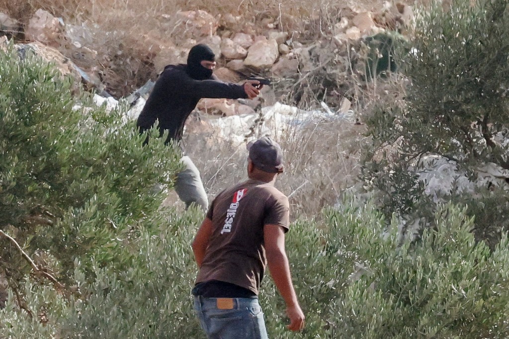 An Israeli settler points a gun amid clashes with Palestinians harvesting olives in West Bank, October 16 (REUTERS)