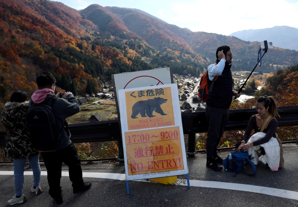 Visitors take souvenir photos next to a bear warning sign at Shirakawa-go, a popular tourist spot and one of Japan's UNESCO World Heritage sites, in Shirakawa village, Gifu Prefecture, Japan, November 15, 2025. REUTERS/Issei Kato