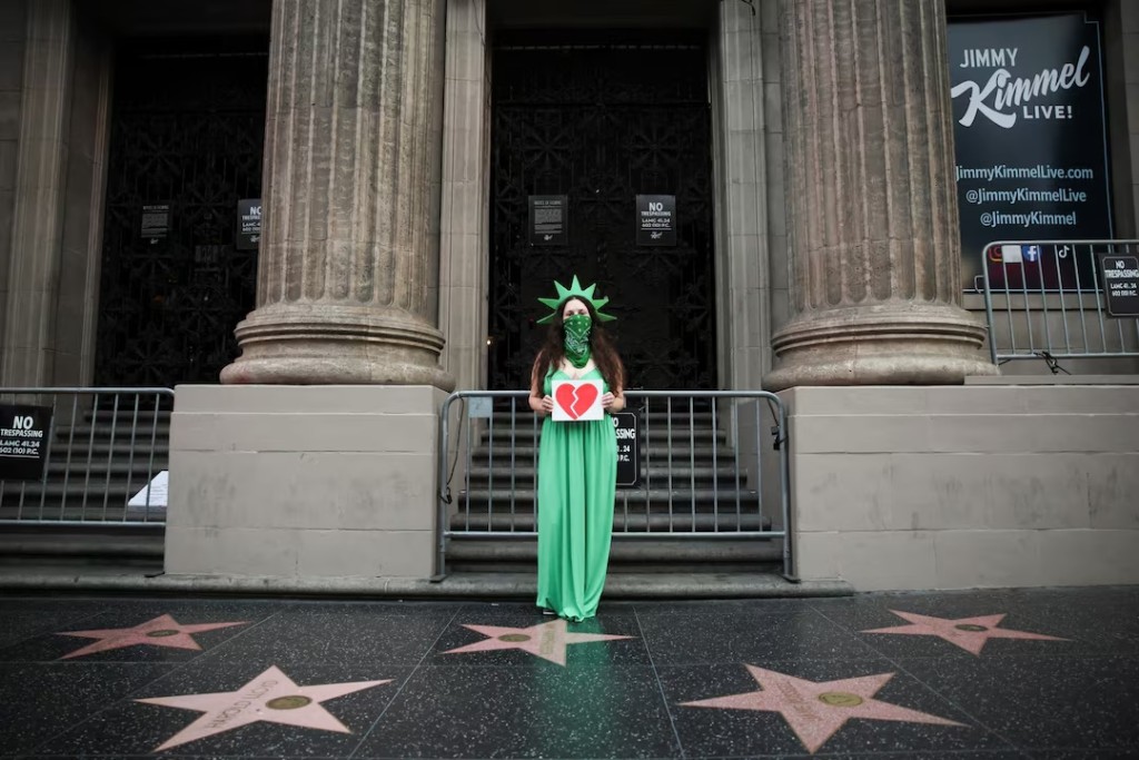 A woman wears a Statue of Liberty costume as she holds an image of a broken heart, outside the El Capitan Entertainment Centre, where "Jimmy Kimmel Live!" is recorded for broadcast, on Hollywood Boulevard in Los Angeles, California, U.S. September 17, 2025. REUTERS/Daniel Cole 