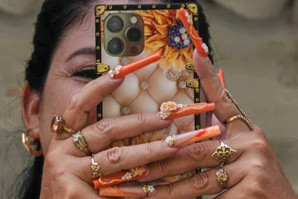 Miralys Maura Cruz sports long, decorative nails as she chats on her phone at home in La Gallega, Havana province, Cuba, Saturday, June 28, 2025. (AP Photo/Ramon Espinosa)