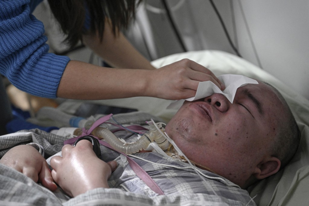 Photo by JADE GAO / AFP  This photo taken on December 16, 2025 shows Li Qian wiping tears for her elder brother Li Xia, who has Duchenne muscular dystrophy, at their house in southwestern China's Chongqing municipality.
