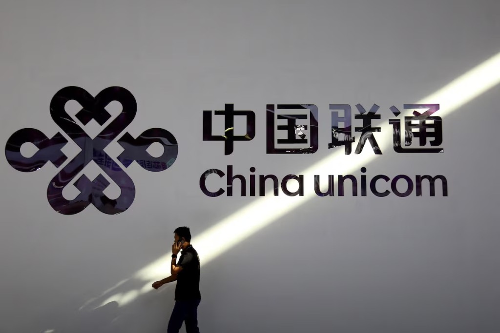 A man holding a mobile phone walks past a China Unicom logo during the Mobile World Congress in Shanghai, China June 28, 2023. REUTERS