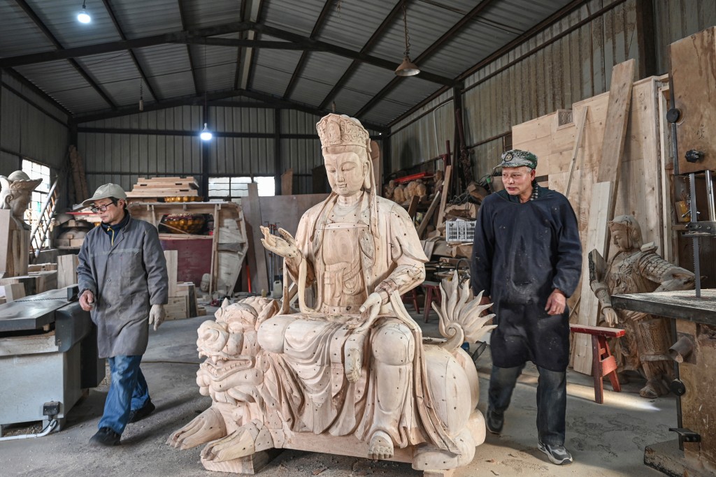 Two artisans walk past a wooden Buddhist figure sculpture at a workshop at Chongshan village in Suzhou, in eastern China's Jiangsu province. (AFP)