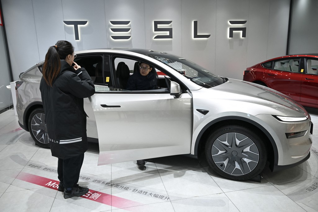 Photo by PEDRO PARDO / AFP  A woman opens the door for a Tesla Model YL electric vehicle as a customer looks inside at a showroom in Beijing on February 3, 2026.