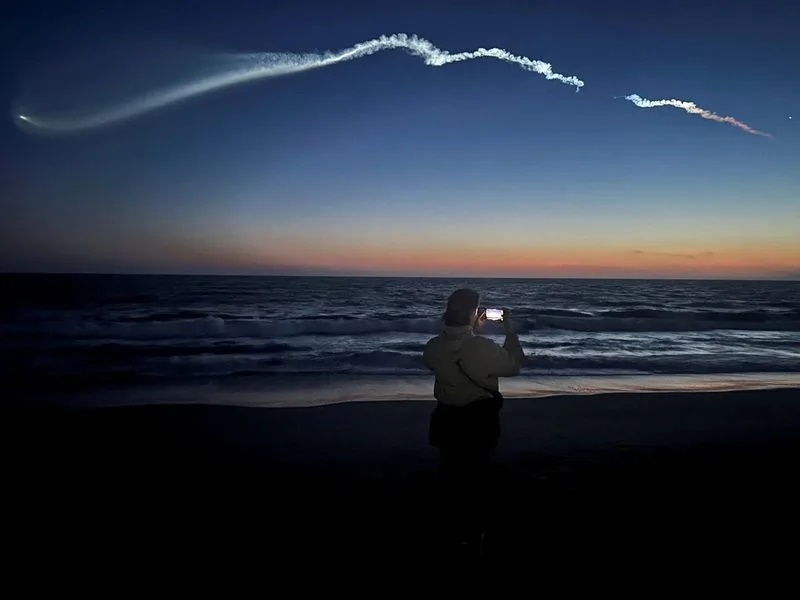 FILE PHOTO: A person takes photos of a trail as the Falcon 9 carrying Starlink satellites streaks across the sky in the latest SpaceX launch as viewed from Venice Beach in Los Angeles, California, U.S., April 6, 2026. REUTERS/Daina Beth Solomon/File Photo