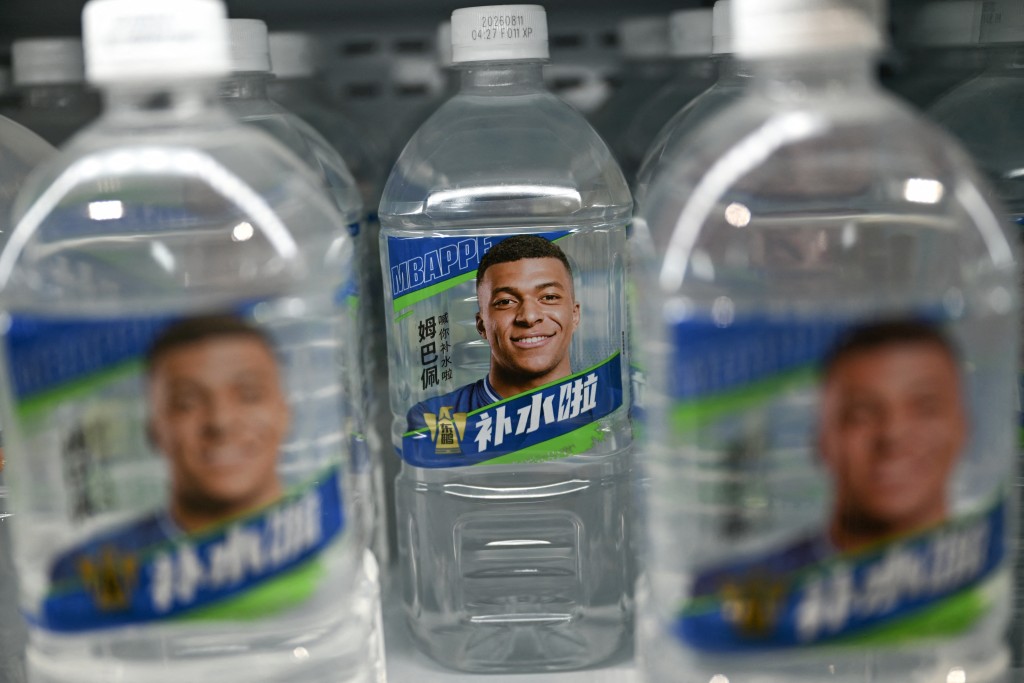 Photo by PEDRO PARDO / AFP  Bottles of Dongpeng Beverage Group's "Bushuila" electrolyte drink featuring French football star Kylian Mbappe on the packaging are displayed at a convenience store in Beijing on October 27, 2026.