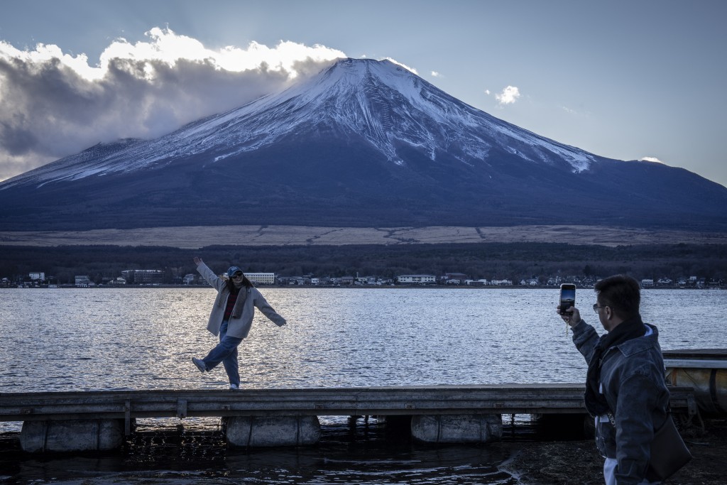 Photo by YUICHI YAMAZAKI / AFP  People take photographs with Mount Fuji at Lake Yamanakako in Yamanakako, Yamanashi prefecture on December 5, 2025.