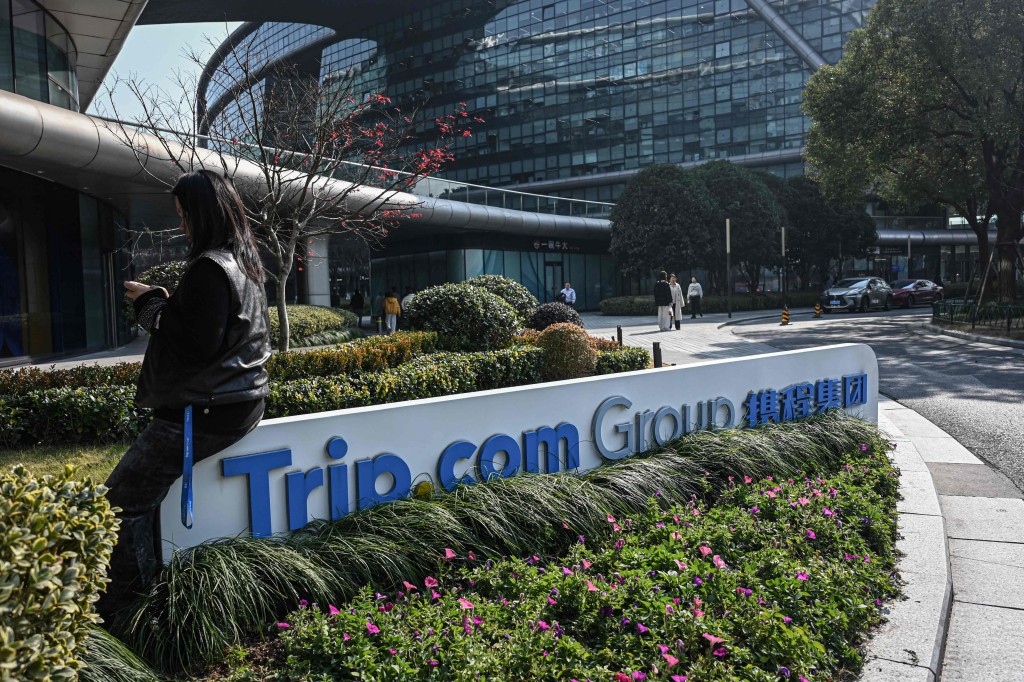 A woman sits on a signage of China's travel agency Trip.com Group at its headquarter in Shanghai on January 15, 2026. AFP