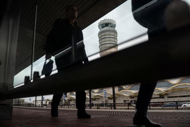 Travelers walk near the air traffic control tower at Reagan Washington National Airport as the U.S. government shutdown continues in Arlington, Virginia, U.S., October 8, 2025. REUTERS/Nathan Howard