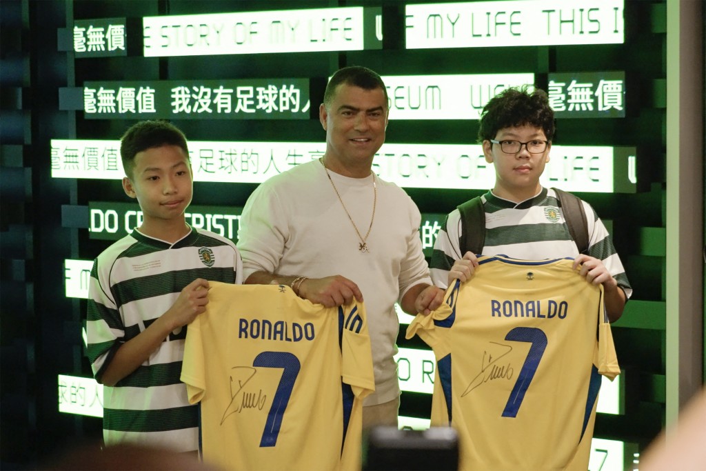 Two fans receiving autographed Cristiano Ronaldo jerseys while posing with the footballer's brother Hugo dos Santos Aveiro (C) during the opening of the CR7 LIFE Museum in Hong Kong on July 7, 2025. (AFP)