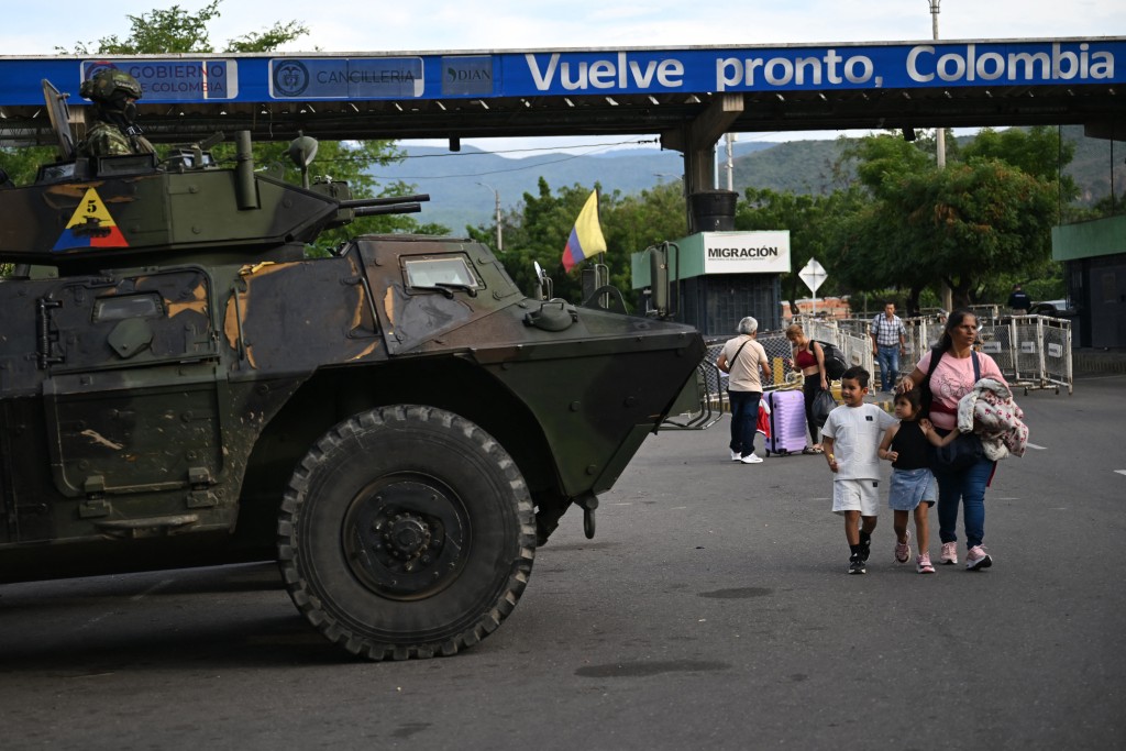 A woman with two kids walks past a military vehicle at the border crossing with Venezuela in Cucuta, Colombia, on January 3, 2026, after US forces captured Venezuela's President Nicolas Maduro. (AFP)