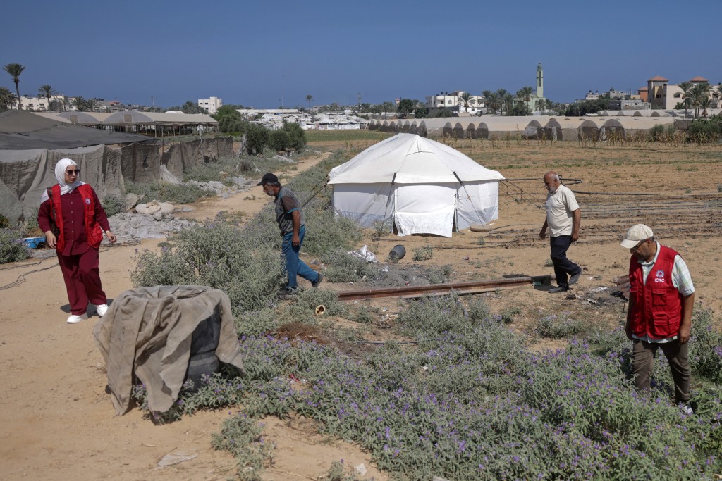Photo by BASHAR TALEB / AFP  Amani Al-Naouq (L), spokesperson for the International Committee of the Red Cross (ICRC) in Gaza, agricultural engineer Abdel Moneim Ahmed (2L) and Osama Al-Mukhalalati (R) an economic security officer with ICRC walk through a field near the Al Qarara Seed Bank, in Deir el-Balah, central Gaza Strip on August 11, 2026.