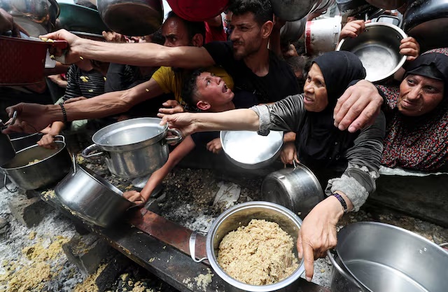 Palestinians wait to receive food cooked by a charity kitchen, in Jabalia, in the northern Gaza Strip, May 14, 2025. REUTERS/Mahmoud Issa
