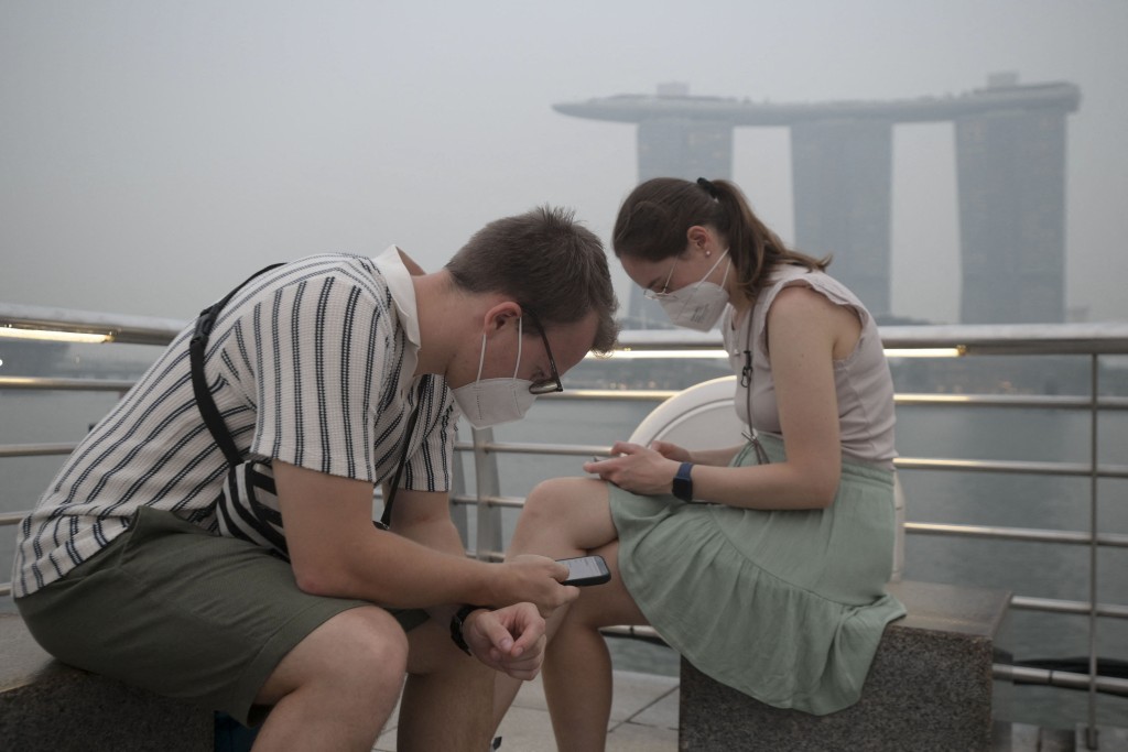 Photo by FELINE LIM / AFP  Tourists wear protective masks while seated across Marina Bay Sands in Singapore on October 15, 2026, as the country continues to be shrouded in haze caused by fires in Indonesia.