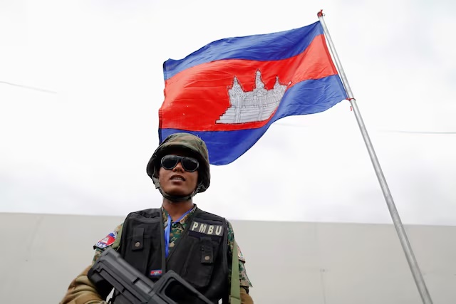 An armed security guard stands under a Cambodian flag in the capital Phnom Penh, November 16, 2012. REUTERS/Damir Sagolj/File Photo