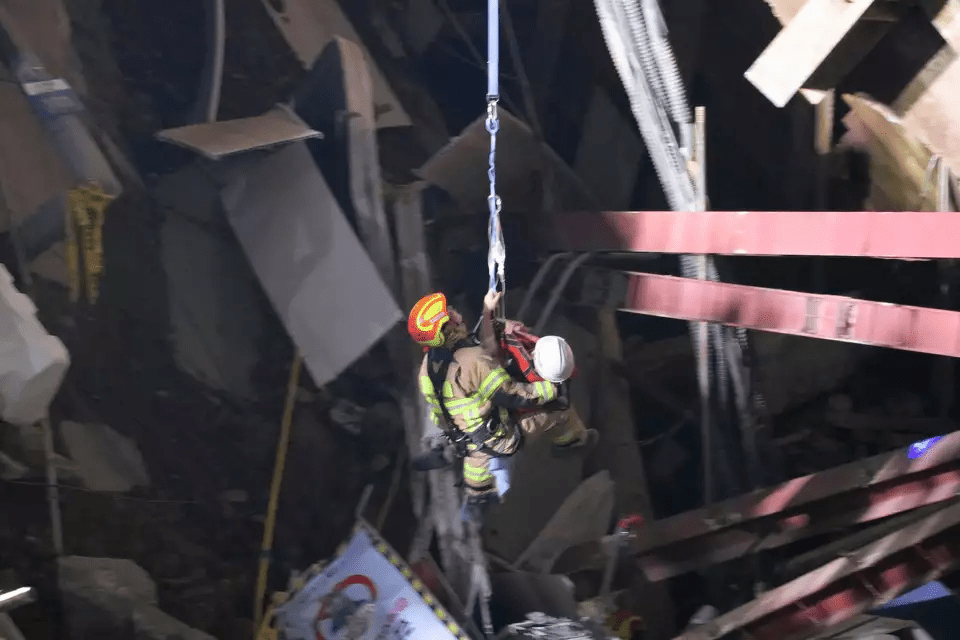 In this photo provided by South Korea Gyeonggi-do Fire Services, a survivor wearing white helmet, is rescued by a firefighter at the scene of a collapsed subway construction site in Gwangmyeong, South Korea, Saturday, April 12, 2025. (South Korea Gyeonggi-do Fire Services via AP)