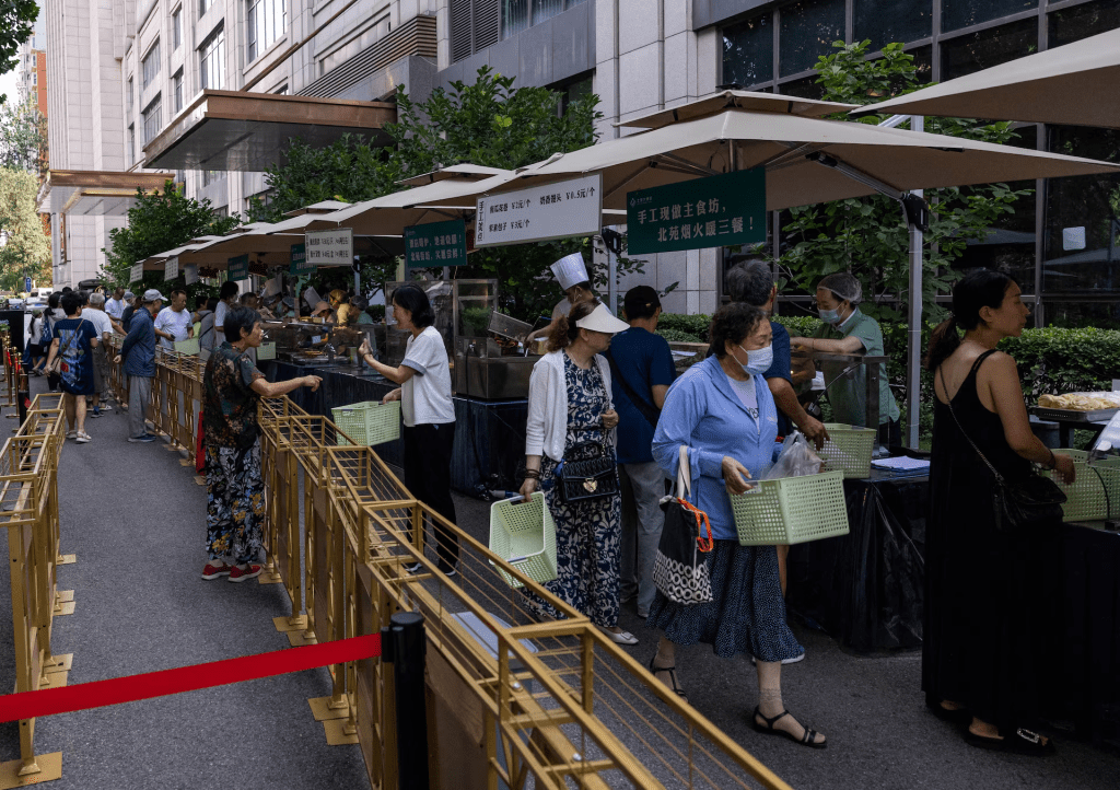 People gather near a setup of stalls selling food to passersby next to Beiyuan Grand Hotel in Beijing, China August 11, 2025. REUTERS/Maxim Shemetov