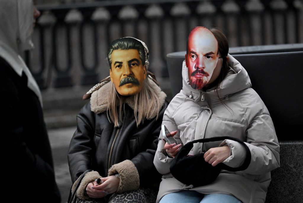 Young women wearing masks of Soviet dictator Josef Stalin and Soviet state founder Vladimir Lenin attend a street musicians' concert in the center of Saint Petersburg on October 27, 2025. (Photo by Olga MALTSEVA / AFP)