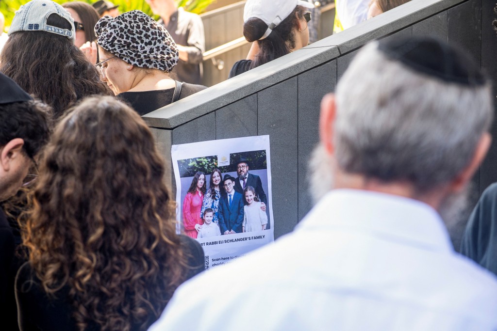 Photo by JEREMY PIPER / POOL / AFP  Mourners watch a live feed of the funeral of rabbi Eli Schlanger, who was killed in the December 14 Bondi beach shooting attack, outside the Chabad of Bondi Synagogue in Sydney on December 17, 2025.