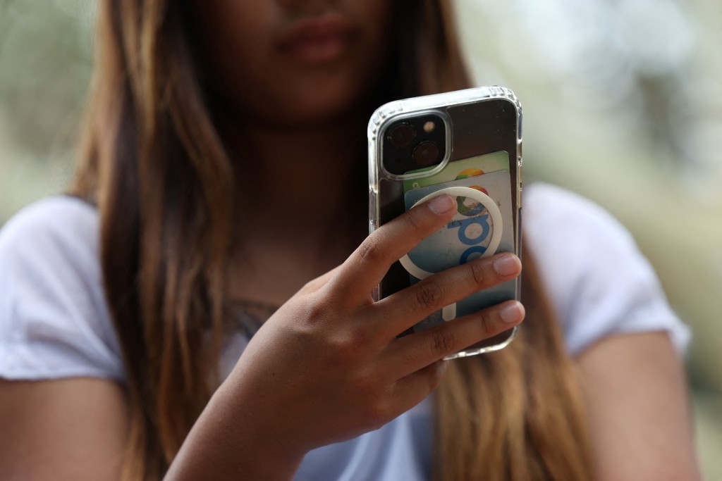 A teenager poses holding a mobile phone as law banning social media for users under 16 in Australia takes effect, in Sydney, Australia, December 10, 2025. REUTERS/Hollie Adams
