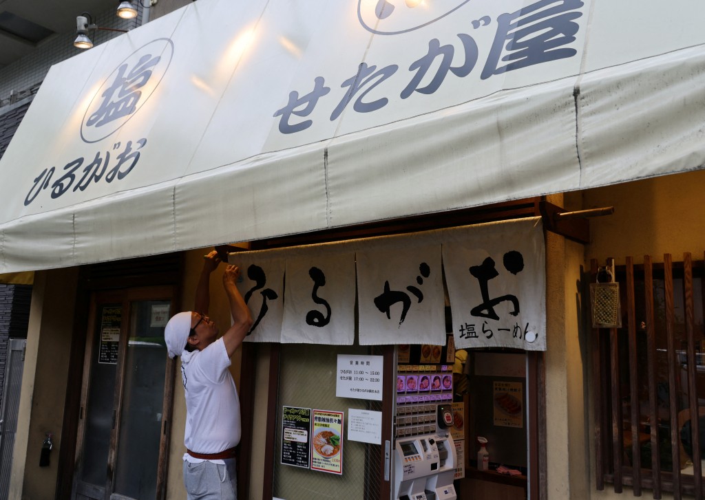 An employee of Setagaya, a Yoshinoya-affiliated ramen company, arranges a noren, traditional Japanese fabric curtain, at the entrances of its shop in Tokyo, Japan, May 19, 2025.   REUTERS/Kim Kyung-Hoon