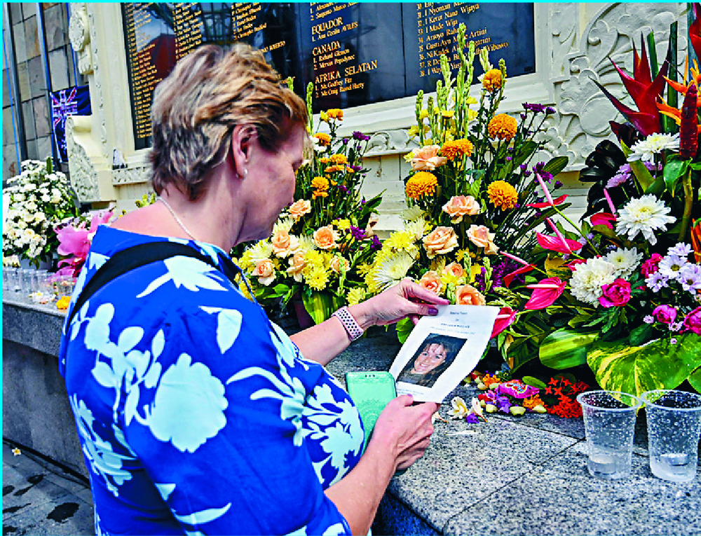 A woman visits the memorial in Kuta honoring the victims of the Bali bombings, survivor Andrew Csabi makes a flower offering on the 20th anniversary of the tragedy and the relative of a victim arrives wearing a shirt with photos of the people killed.